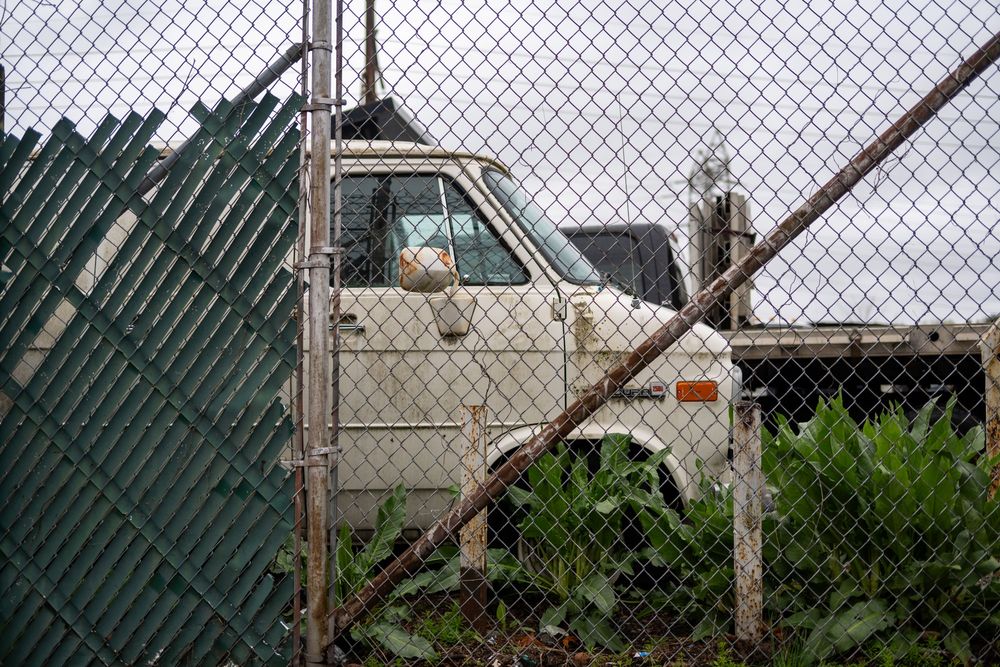 Beaten up chevy van behind a rusty fence and weeds