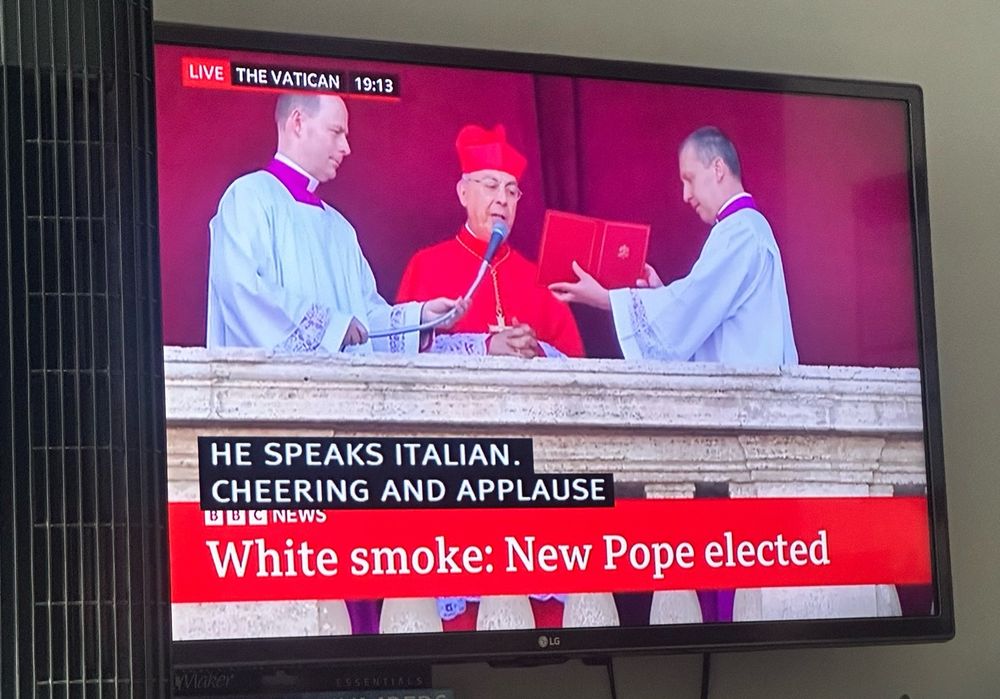 my tv showing bbc live coverage of the proto-deacon announcing the new pope with the subtitles "HE SPEAKS ITALIAN. CHEERING AND APPLAUSE"