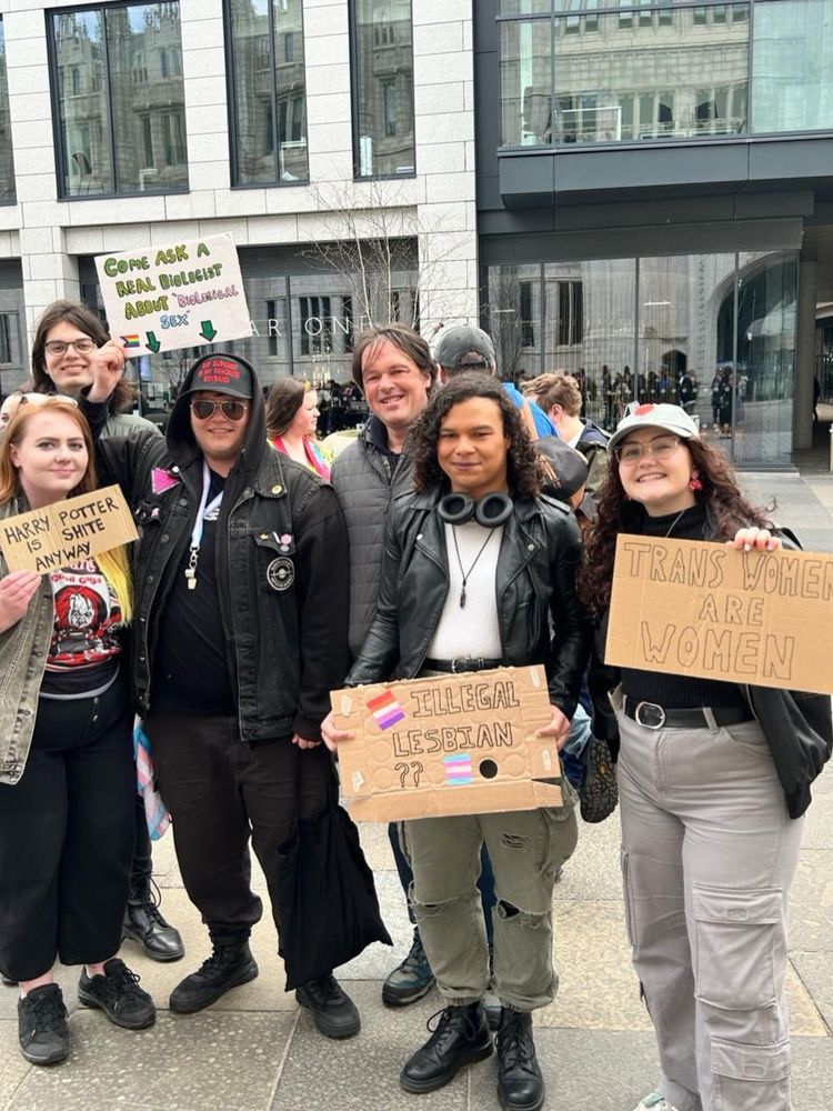 6 people at the protest, myself included, holding various signs. from left to right, the signs read: "harry potter is shite anyway" "come ask a real biologist about "biological sex"" "illegal lesbian??" and "trans women are women"