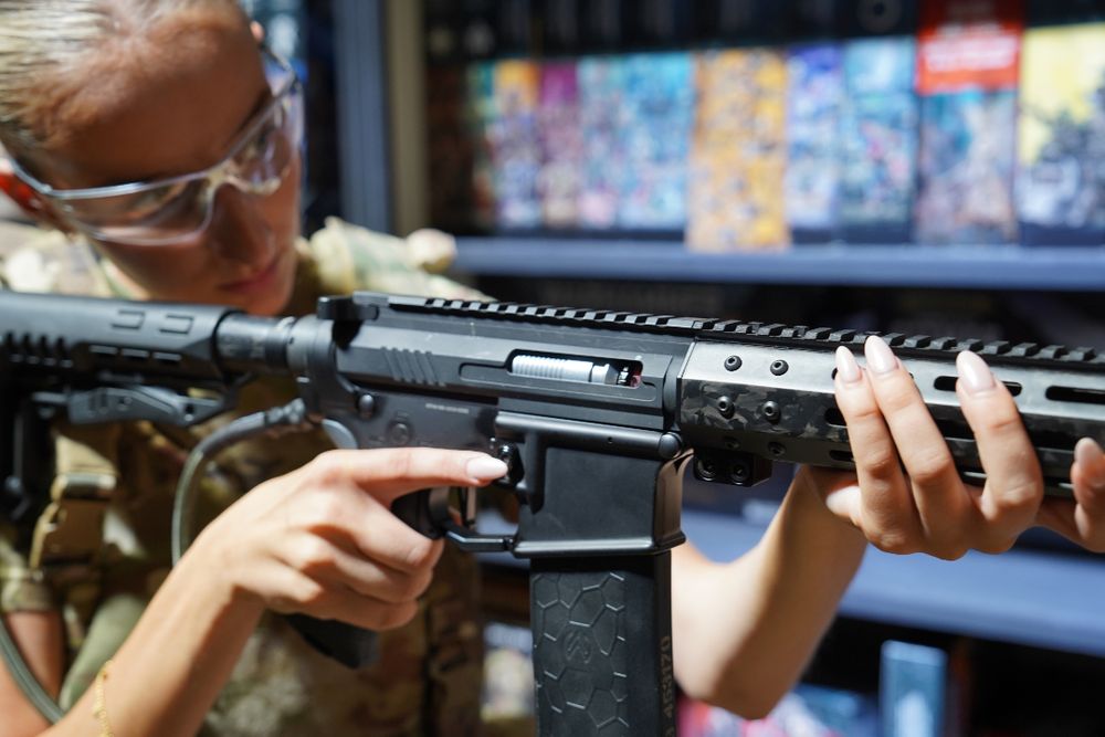Close-up of a custom Gen 1 Wolverine MTW being aimed, showing OG Carbon handguard, CNC trigger, and internal bolt detail in a well-lit shop environment.
