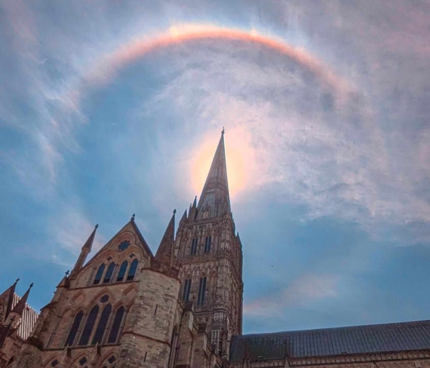a rainbow circles the top of the spire as the sun shines behind it