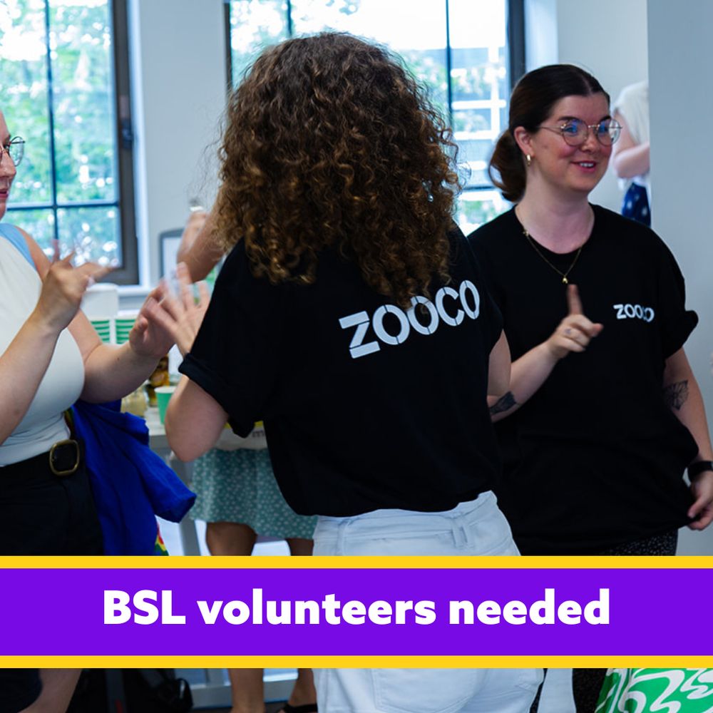 Three people in black "ZOO CO" t-shirts signing British Sign Language in a room with large windows. Text reads "BSL volunteers needed" on a purple banner below.

