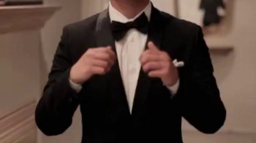 a man wearing a tuxedo and bow tie is adjusting his jacket .