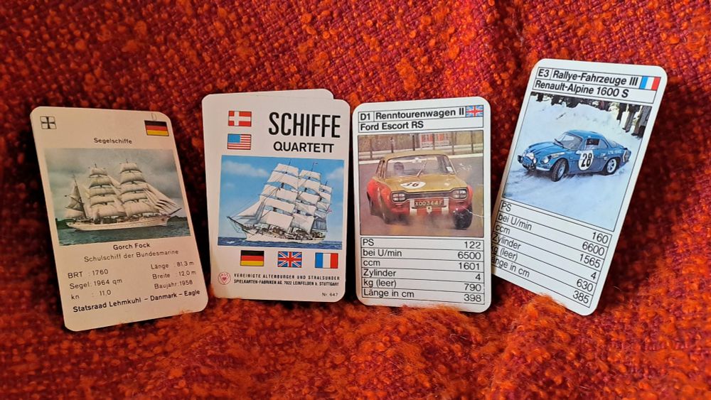 Auf einem alten Clubsessel mit einem orangefarbenen Boucléstoff liegen 4 Quartettkarten. Links die Gorch Fock mit technischen Angaben. Daneben das Deckblatt des Schiffe Quartetts und auf der rechten Seite 2 Karten eines Rallyefahrzeuge Quartetts, ein Ford Escort und ein Renault Alpine.