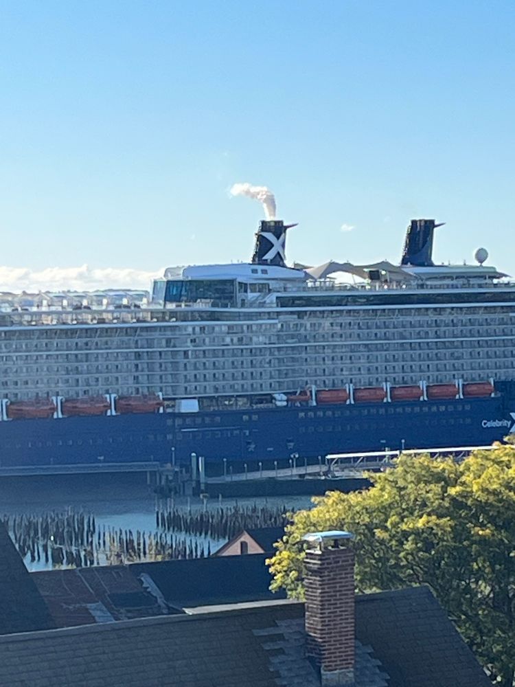 A detail image of a cruise ship in Portland Maine spewing emissions from its exhaust. With historic pilings and roof tops in the foreground. 