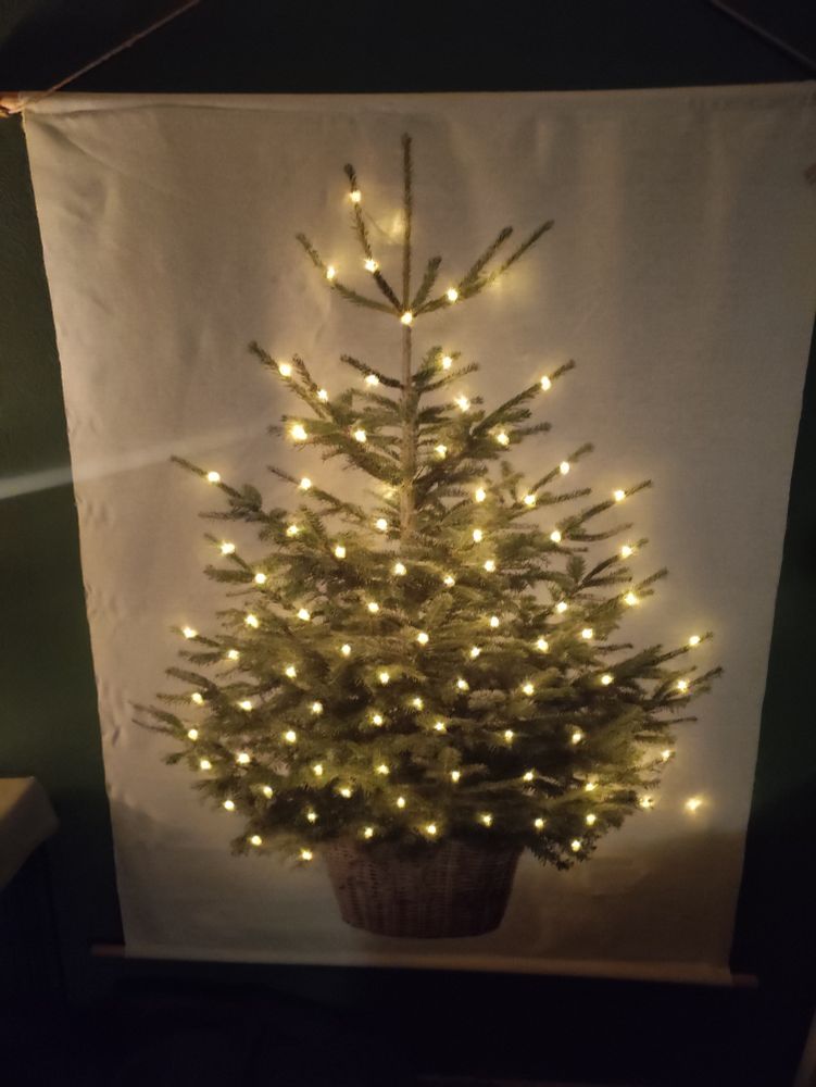 Een wanddoek met daarop de afbeelding van een kerstboom en de lampjes schijnen er doorheen. 