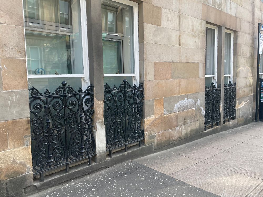 Decorative cast-iron grilles fitted to protect pavement-level windows in Glasgow.