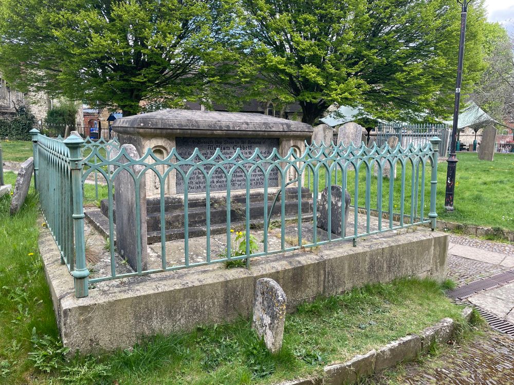 The grave of William Cobbett in Farnham. The large free-standing chest tomb, in ?greensand with a granite inscription slab, stands on a substantial rectangular plinth, around the edge of which is set iron railings with decorated corner posts. The ironwork is in excellent condition and has been painted in a blue-green colour.