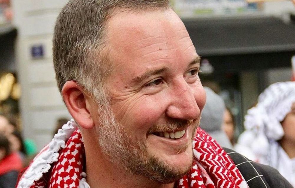 Smiling Jo Daher wearing red & white keffyeh