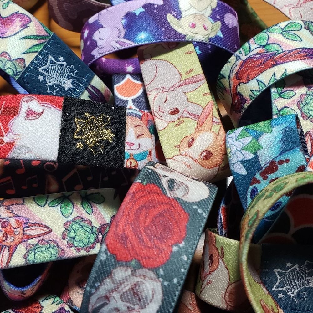 A pile of colorful fabric wrist bands. designs show wolves, bunnies, skulls, roses, koi fish, lambs and other animals and nature motifs
