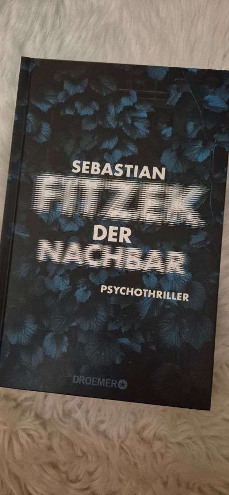 Eine Ausgabe "Der Nachbar" von Sebastian Fitzek auf einem weißen Kunstfell