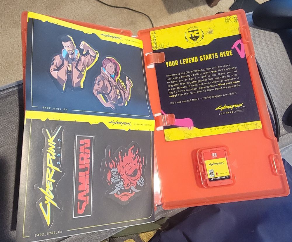 Inside of Cyberpunk 2077 Ultimate Edition for Switch 2. Shows the game cartridge, a sticker set, and a welcome card. 