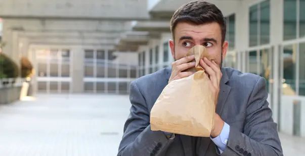 A man having a panic attack and breathing into a paper bag. Or huffing paint, I can't be sure.