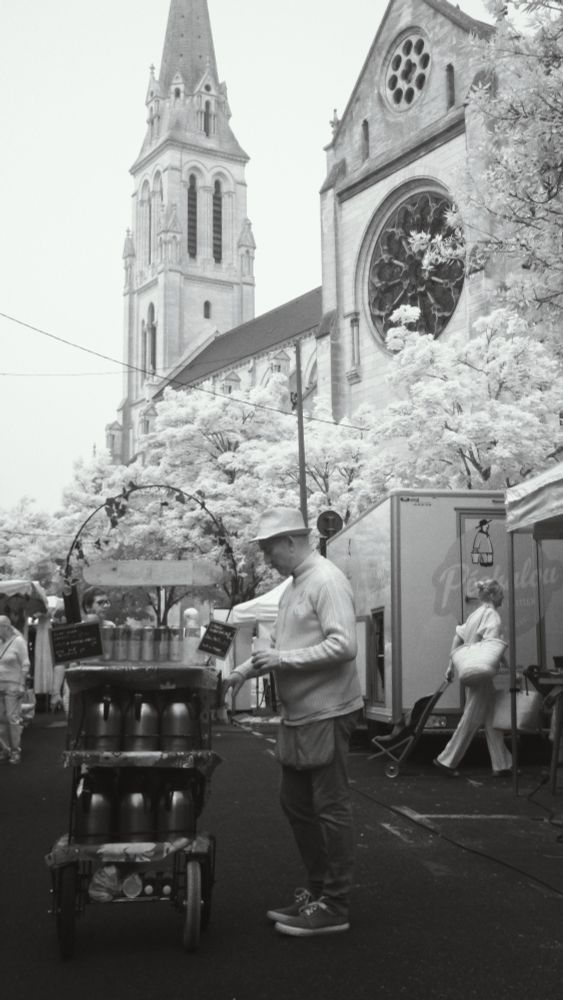 A man with his trolley, selling tea and coffee to stall-holders at a street market. A church is in the background, with trees around the building.