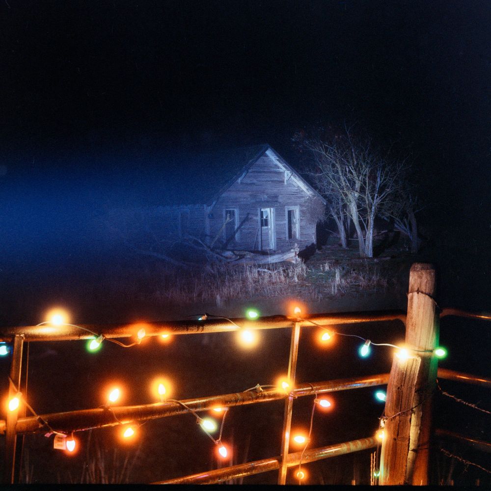 a picture of an abandoned farmhouse and a fence with christmas lights on it. lights and house are both sharp