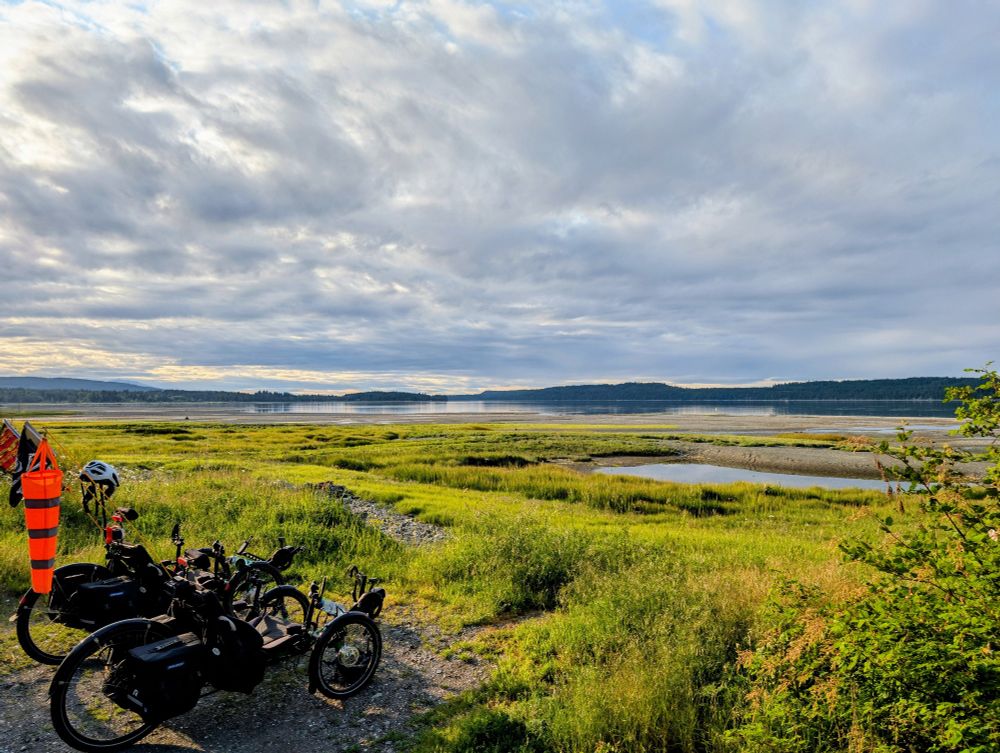 2 recumbent trikes overlooking the beach/shore with the ocean and Denman Island in the background.