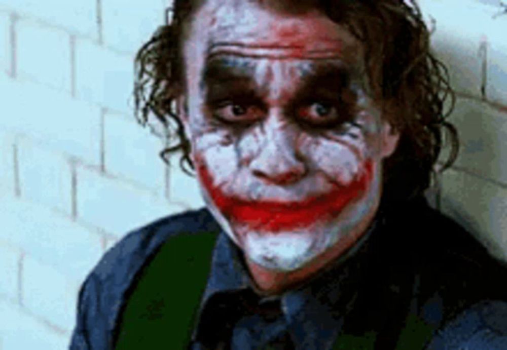 the joker is leaning against a wall with his face painted and making a funny face .