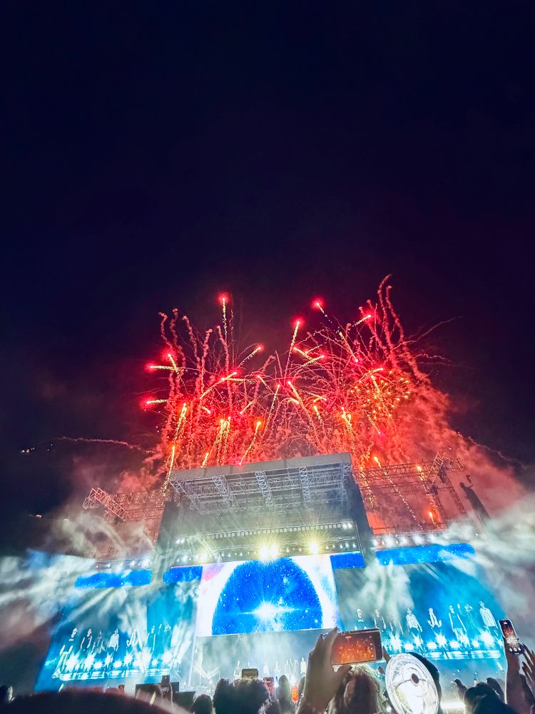 Fireworks lighting up a dark sky behind the stage and screens at the Ateez concert. 