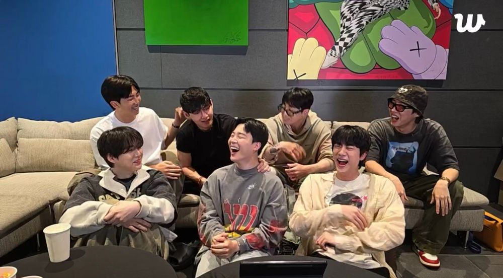 Screenshot of BTS OT7 live from July 1, 2025. They’re seated on a couch/the floor together, and everyone is laughing, especially Jimin and Jin. 