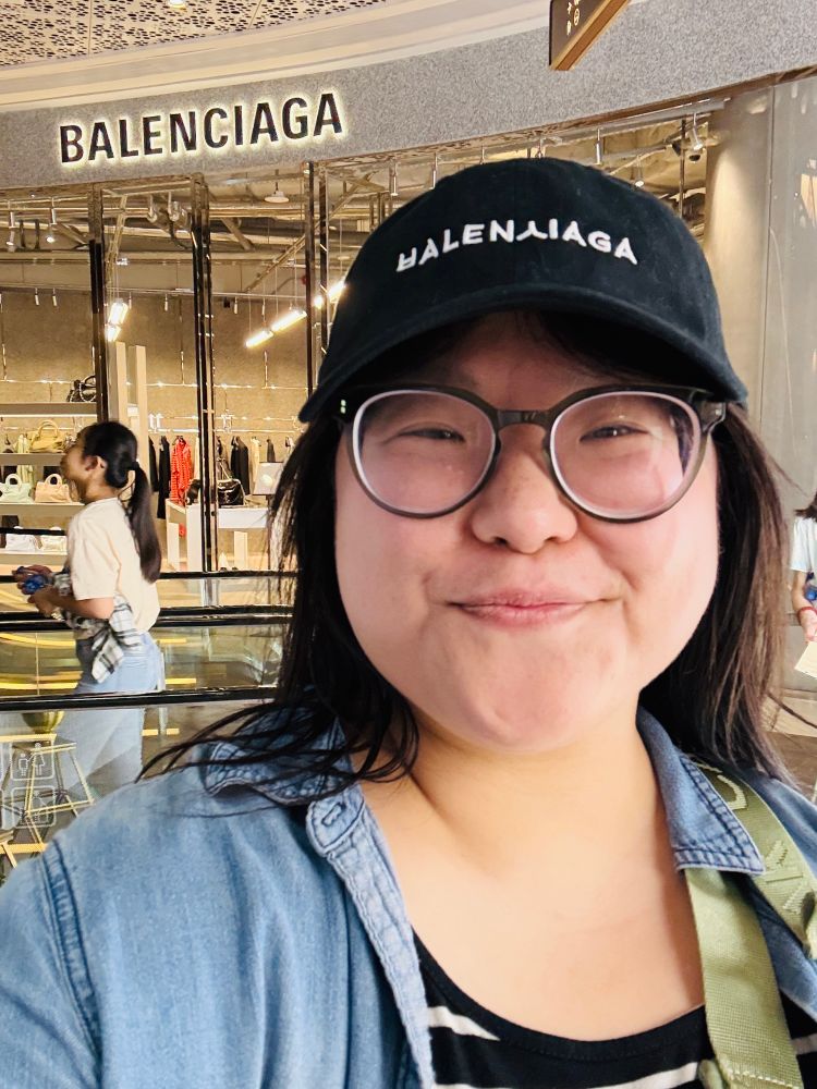 Selfie of me in a chambray shirt and the black “ㅂALENㅅIAGA” ball cap from Anti-Brand, in front of an actual Balenciaga store. 