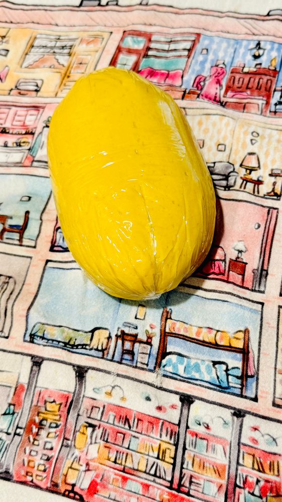 A ball of fairly bright yellow pasta dough, wrapped in plastic on a patterned towel. 