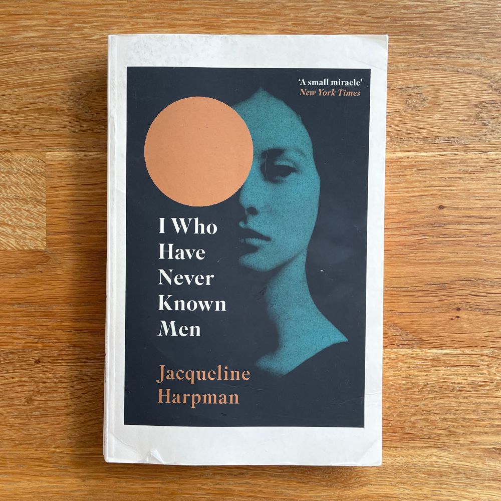 Cover of I Who Have Never Known Men by Jacqueline Harpman. A woman’s silhouette is half hidden behind an orange circle.