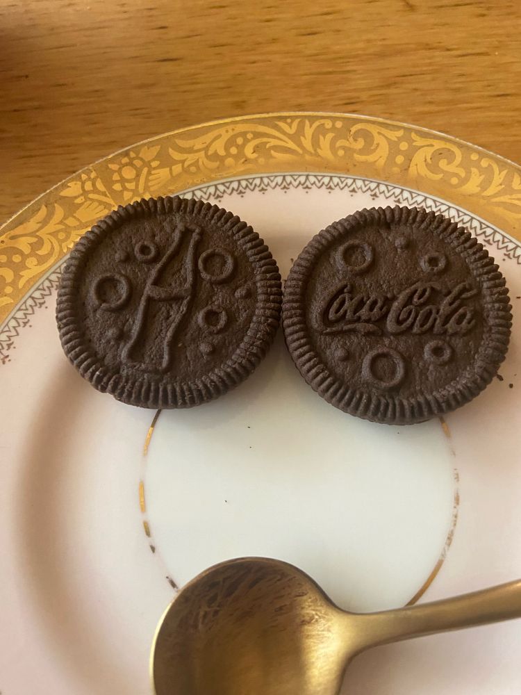 Photo of two coca-cola flavoured oreo biscuits on a plate—one features a cola bottle, the other the coca-cola logo