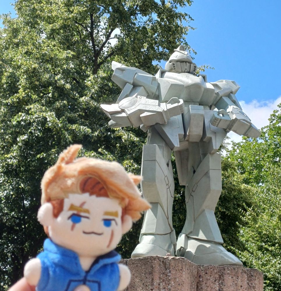 A plushie of Luke posing next to an unofficial Gundam statue in Rotterdam