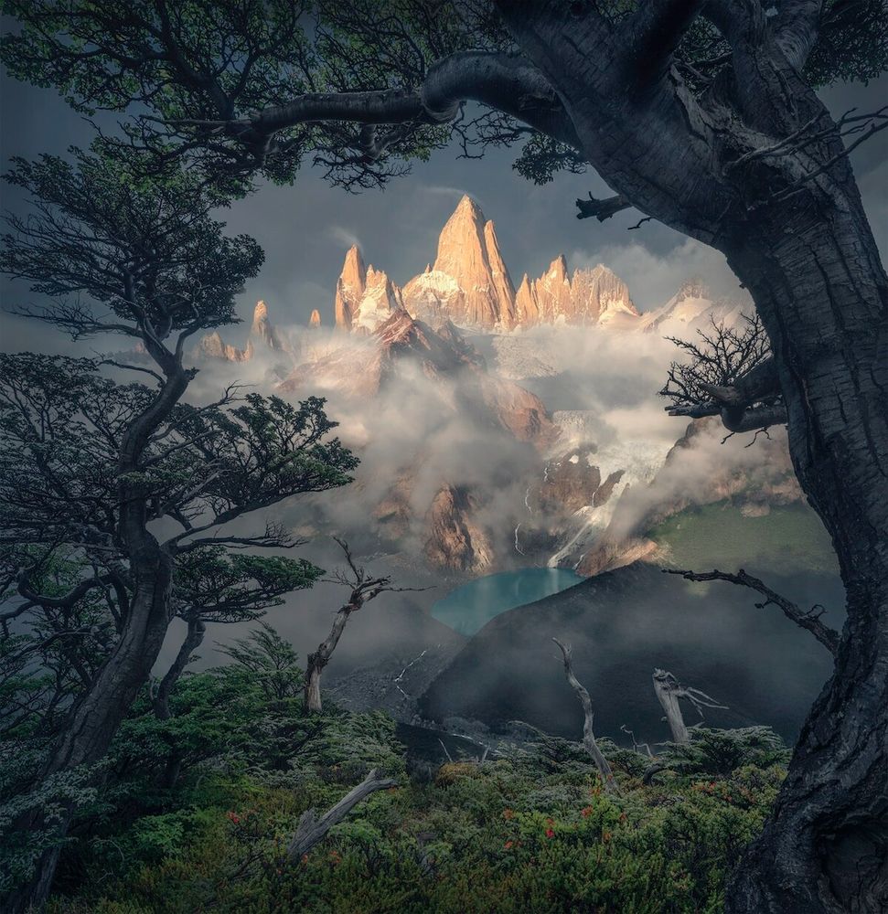 This image is by the photographer Max Rive.

Vast, jagged peaks rise toward the sky. Nestled among their lower reaches is a lake, its water a pristine and depthless blue.