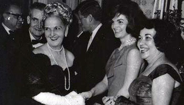 A photograph of San Juan, Puerto Rico Mayor Felisa Rincón de Gautier (1897-1994) meeting American First Lady Jacqueline Lee Kennedy around 1962 at a formal party.  On the far right of the photograph is an unidentified lady appearing with both of them.