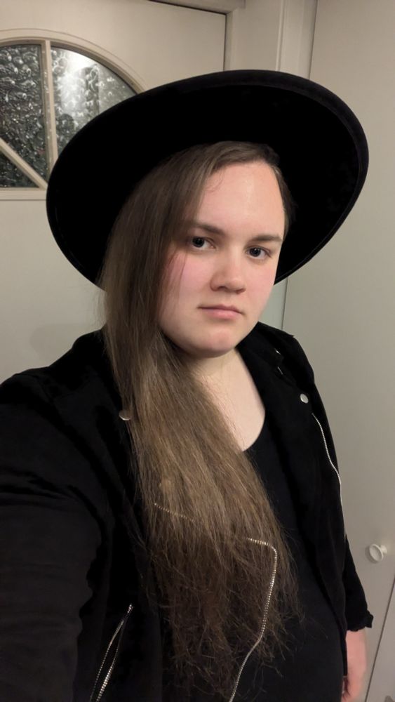 A woman with long hair wearing a fashionable black hat, showcasing her style and personality.