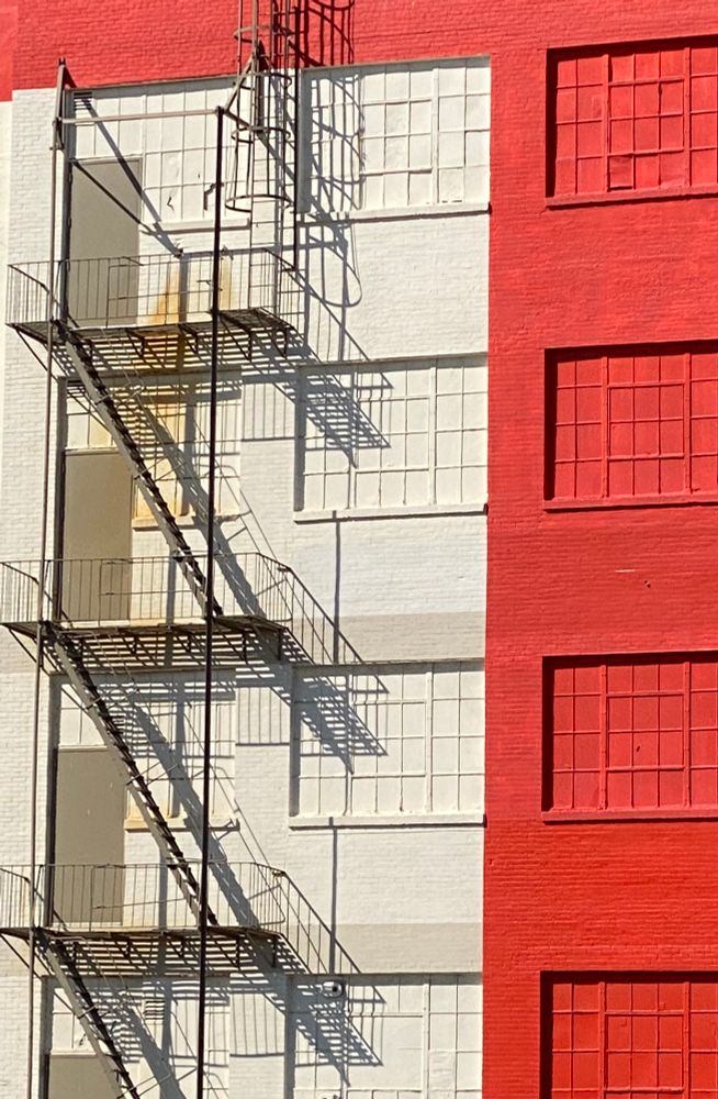 Red building facade next to white building facade with a fire escape. 