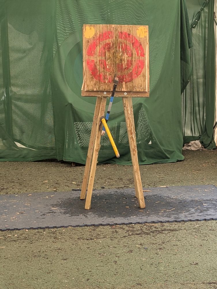 A wooden target with an axe in it and one in the leg