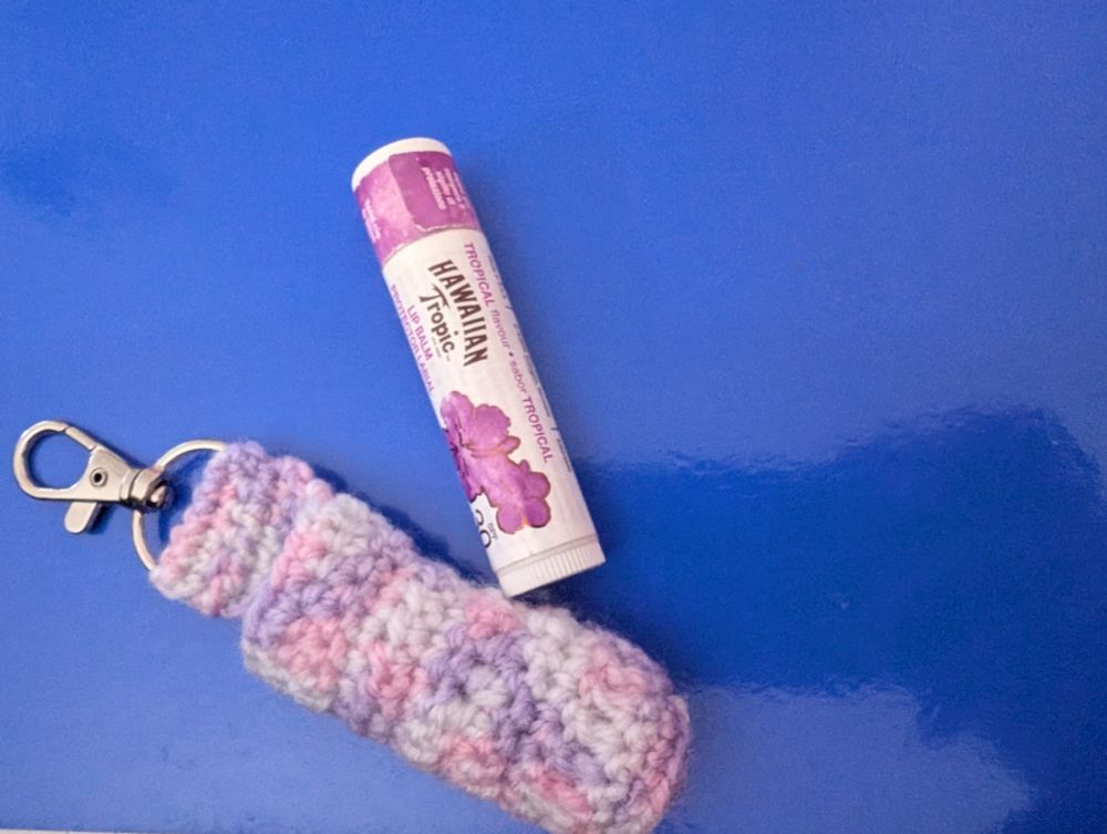 A purple and white Chapstick holder with silver lobster clasp, a purple lidded Hawaiian Tropics Chapstick can be seen beside it.
