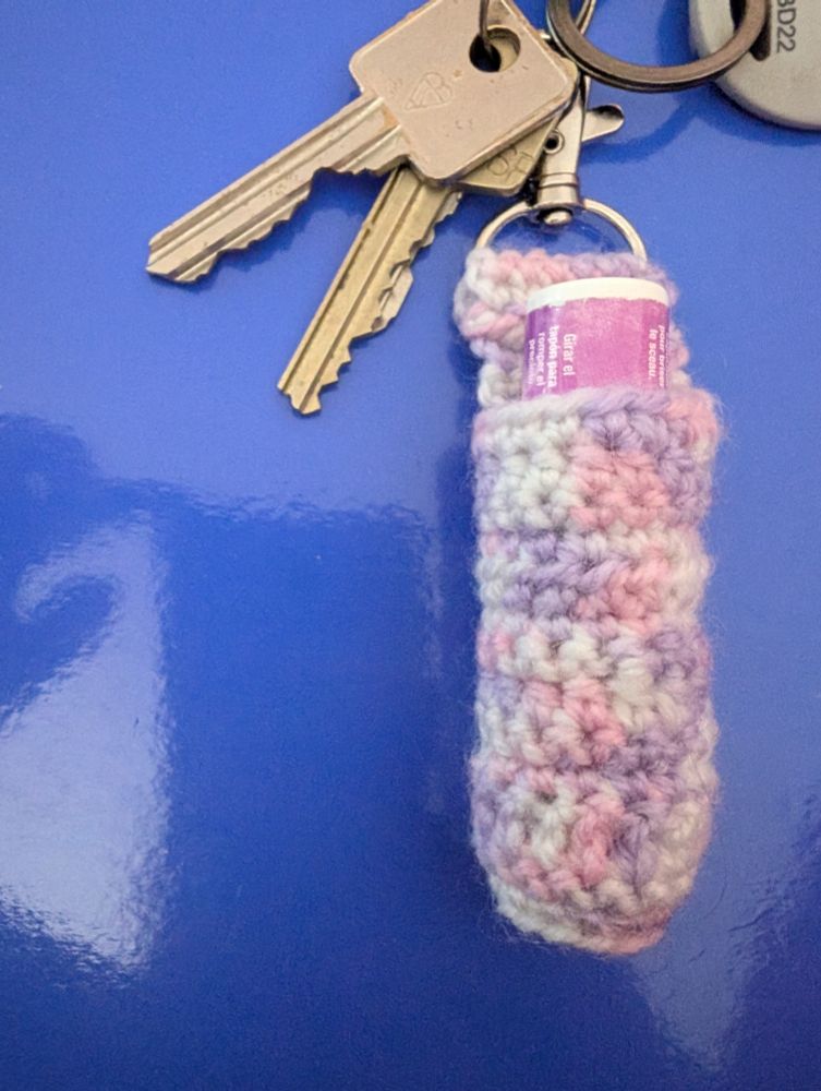A purple and white Chapstick holder with silver lobster clasp, attached to some keys a purple lidded Hawaiian Tropics Chapstick can be seen inside.