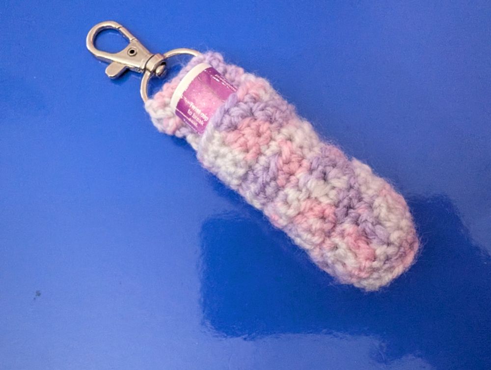 A purple and white Chapstick holder with silver lobster clasp, a purple lidded Hawaiian Tropics Chapstick can be seen inside.