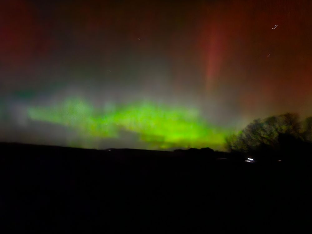 Dark sky lit up by the surreal colours of the northern lights.  Clouds of green and pillars of magenta glow over a dark meadow.
