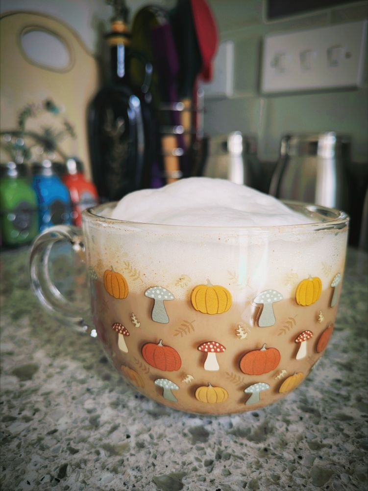 coffee with lots of foam in a clear glass mug with pumpkin, mushroom and fern decals on it