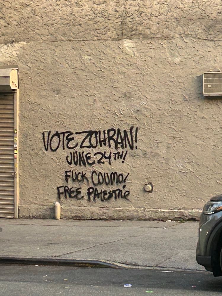 beige wall with black graffiti that reads
‘Vote zohran!
June 24th! 
Fuck cuomo! 
Free Palestine’