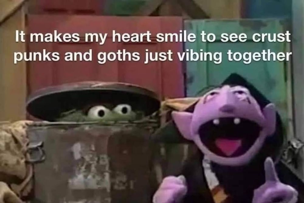 It's a meme involving a screenshot from Sesame Street where Oscar the Grouch is peeking out of his trash can at The Count who is speaking (most likely counting) while facing the viewer. The white text at the top of the image says, "It makes my heart smile to see crust punks and goths just biting together."
