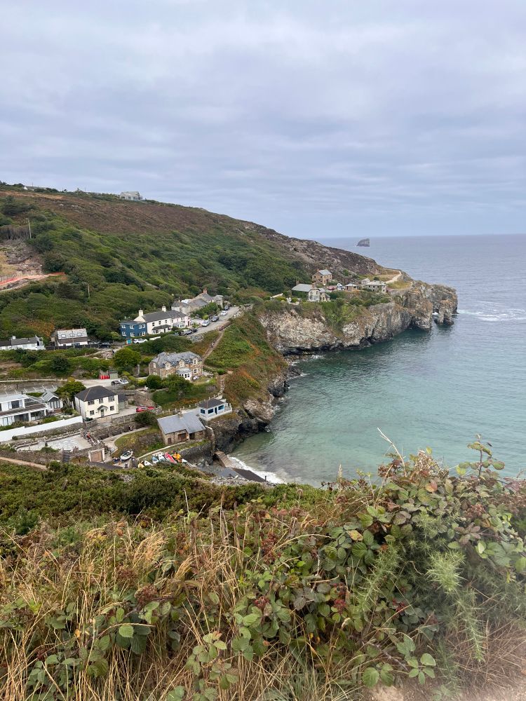 A view over Trevaunance Cove, St. Agnes, showing the ocean, the beach and the village nestled in grassy hills.