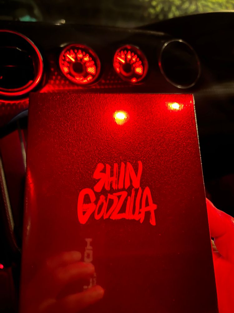 Picture of the Shin Godzilla box, taken in my car under very red lighting conditions. Dashboard gauges are visible in background.