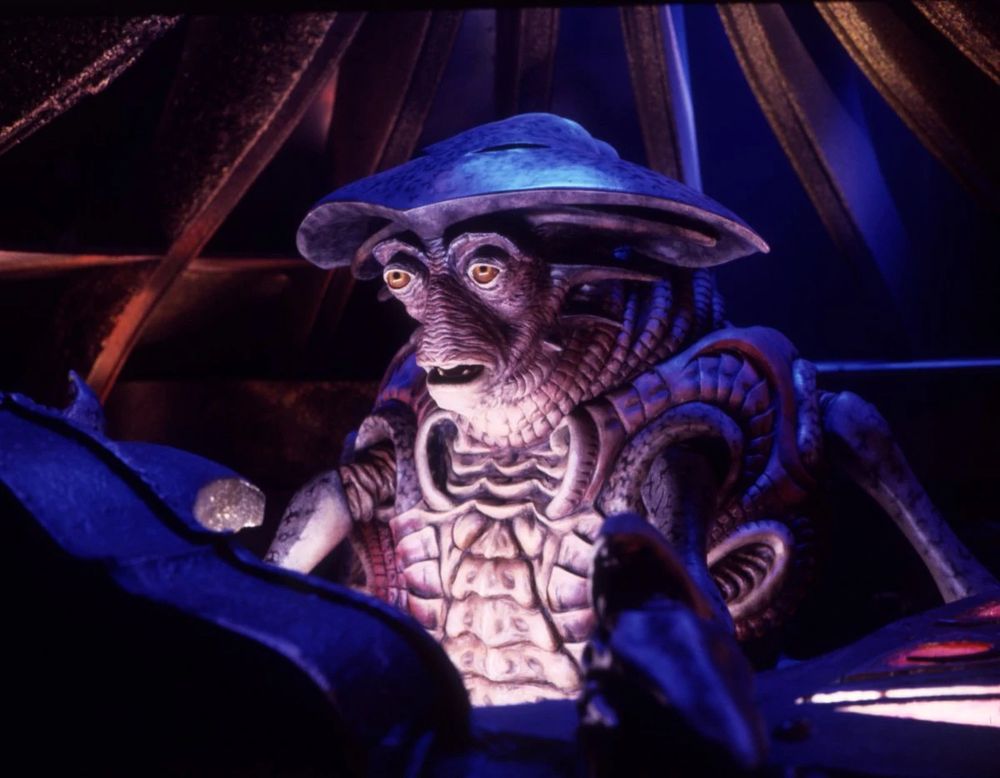 Pilot from Farscape. Pilot is a many armed alien creature whose head sort of resembles a horseshoe crab. They have orange eyes and a chitinous body.