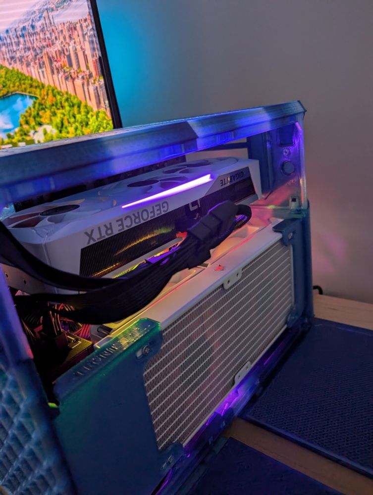 The side of the blue/aqua case has been opened with a view inside of the white graphics card is that has upside down text "GEFORCE RTX" and the radiator of the liquid cooler for the CPU.
