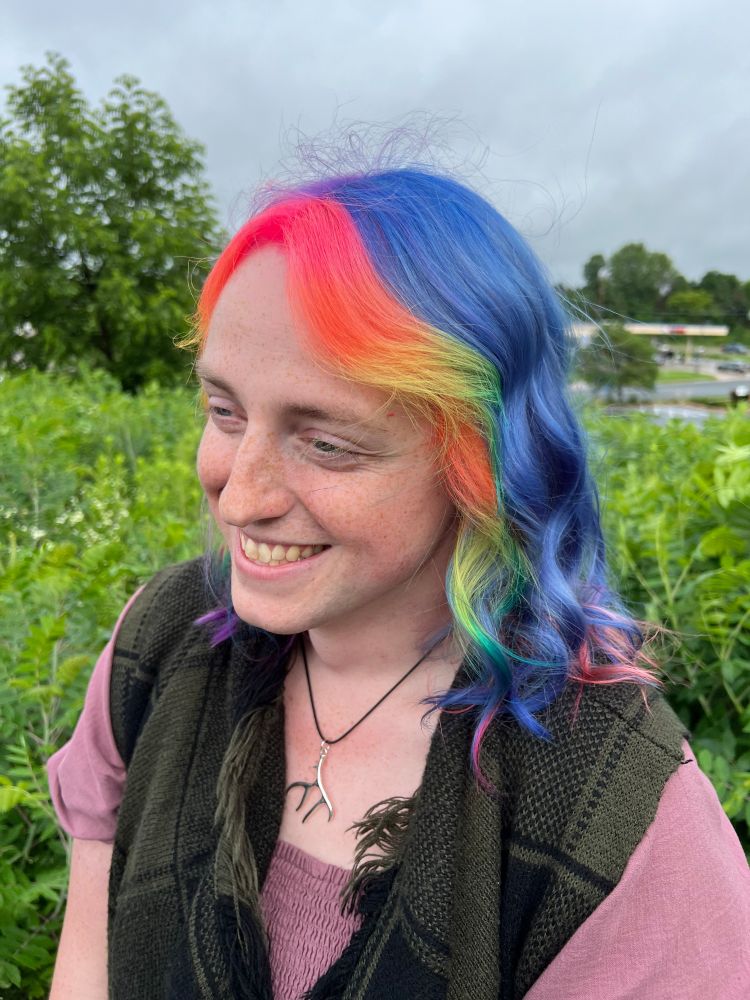 Left side picture that shows off blue hair in the back and the "neon money piece" bangs that are neon colors of a pride rainbow.
