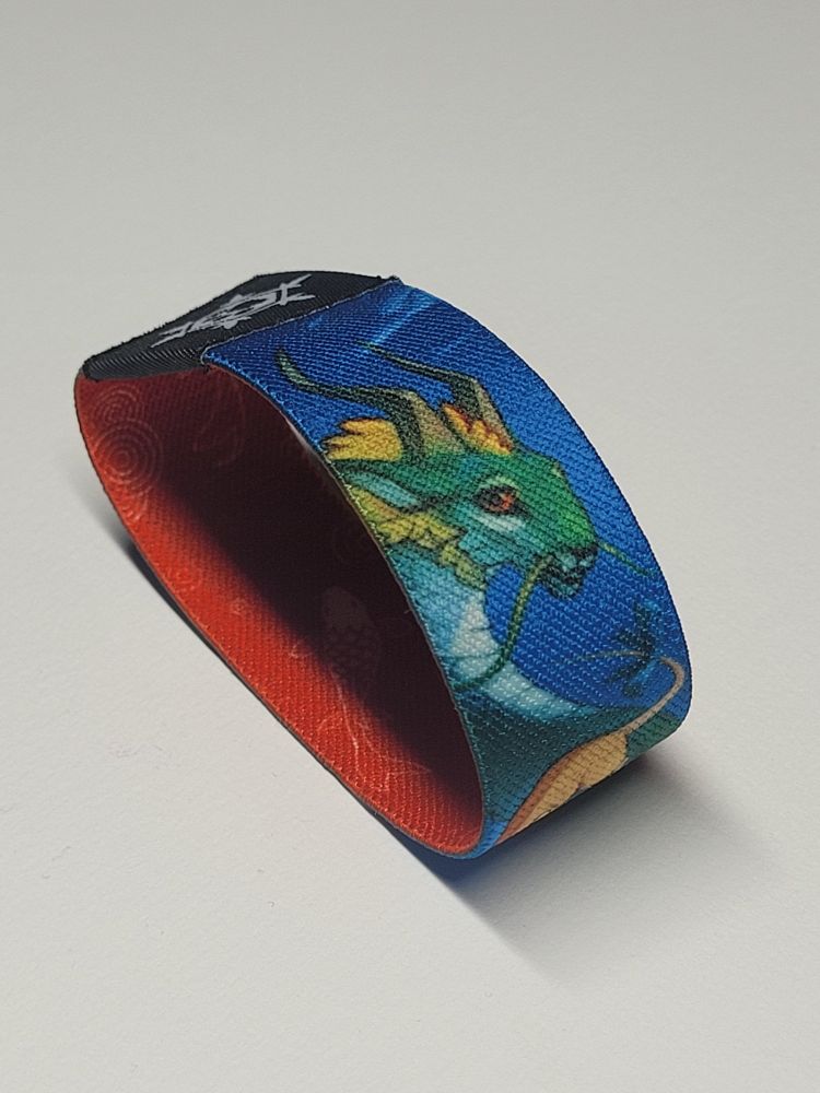 Photo of a wristband on white background. On its outer side is an artwork with the head of a chipper dragon looking at the viewer. Also visible is the inner side of the wristband, featuring an artwork of white fish on red background.