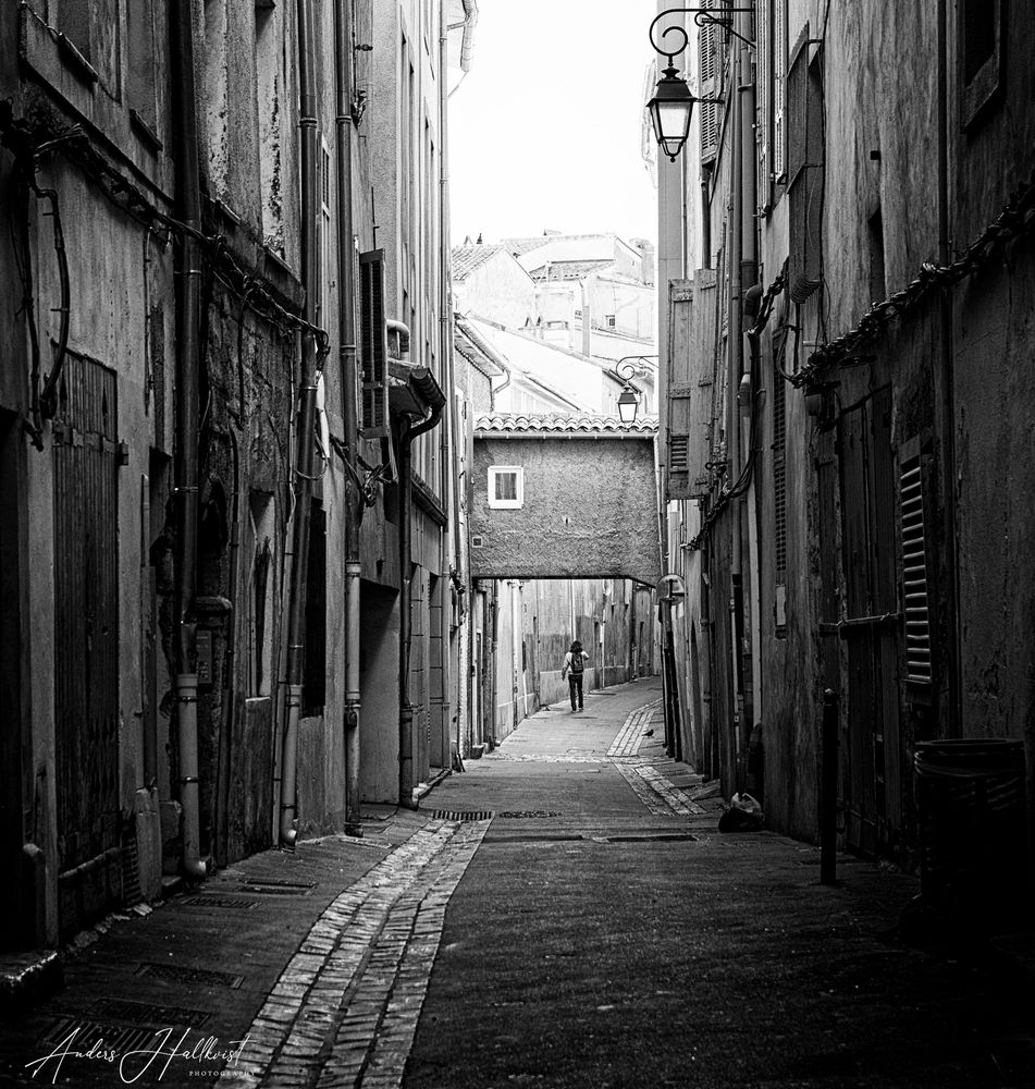Black and white photograph. A person walking in an alley