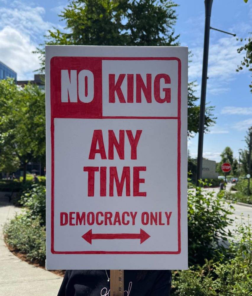 A sign modeled after a No Parking sign which read No King Any Time and Democracy Only on red letters on a white background.