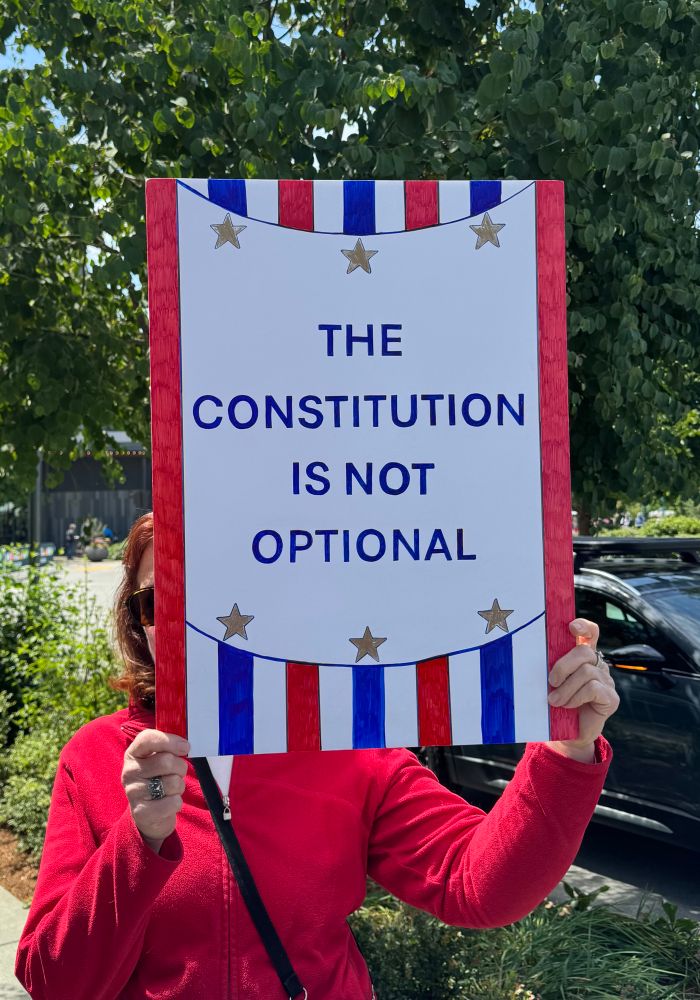 A poster which reads The Constitution is Not Optional in dark blue lettering on a white background. The top and bottom have red, white and blue stripe and three gold stars. The sides have red edges. 