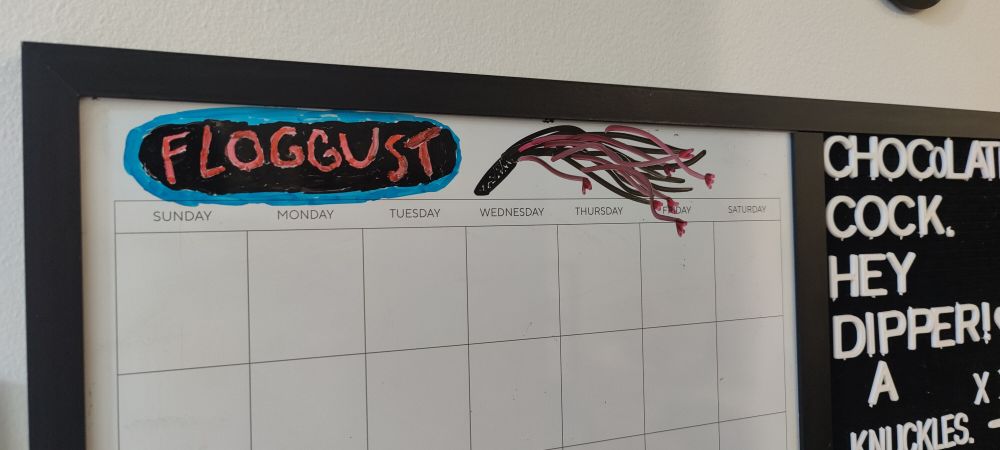 The same whiteboard now having the month set to "Floggust," written with red letters surrounded by black with a light blue outline, similar to a neon open sign. There is a flogger drawn next to it with black and pink as the colors.